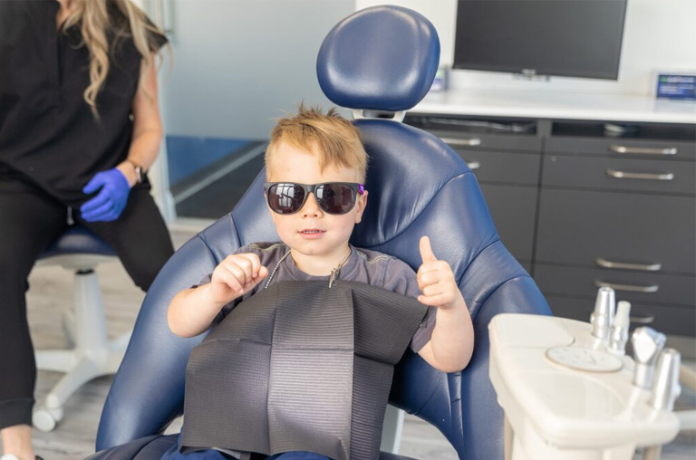 A young boy sitting in a dentists chair with sunglasses on.