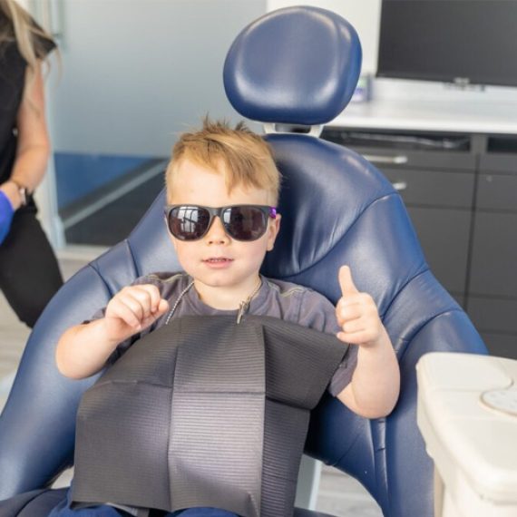 A young boy sitting in a dentists chair with sunglasses on.